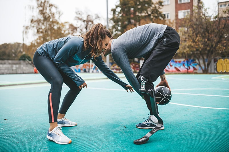 Man with prosthetic leg and woman engaging in a friendly basketball game.
