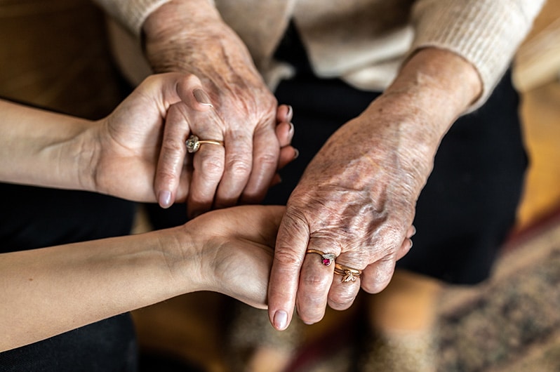 Elderly woman's hands cradled by a younger woman's hands, symbolizing support and connection