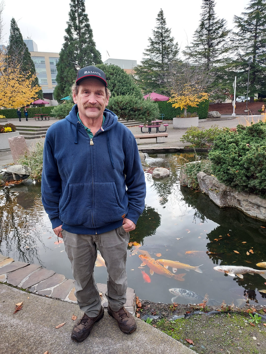 Mike McDonald standing in front of a koi pond with large fish visible in the water.